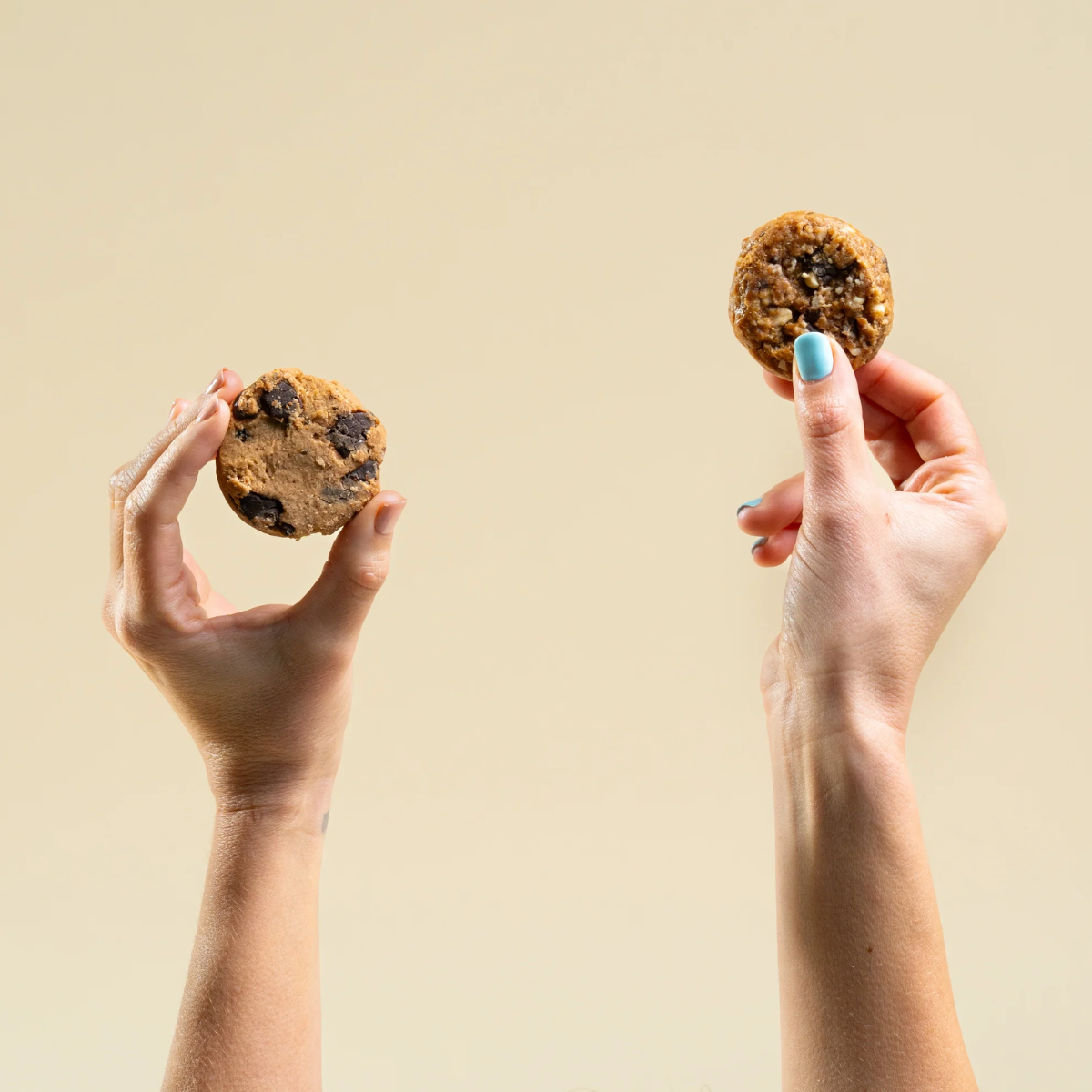 Two hands holding two cookies against a beige background