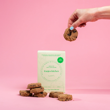 Hand holding a cookie above a box of 'frankies kitchen' lactation biscuits on a pink background
