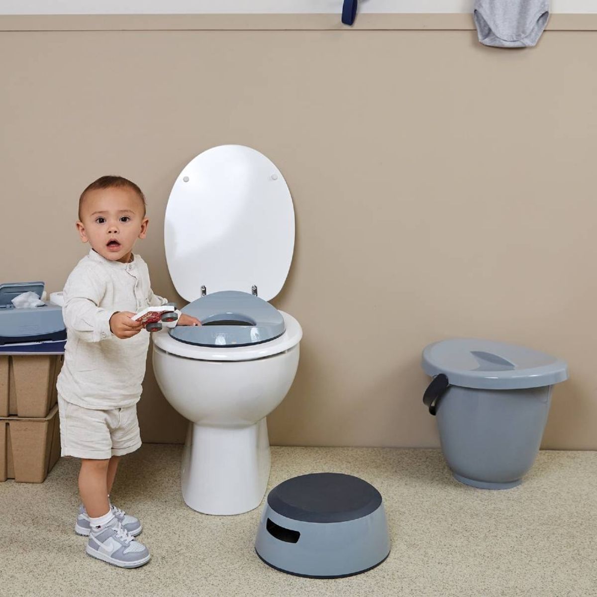 Child standing next to a toilet with various bathroom items around