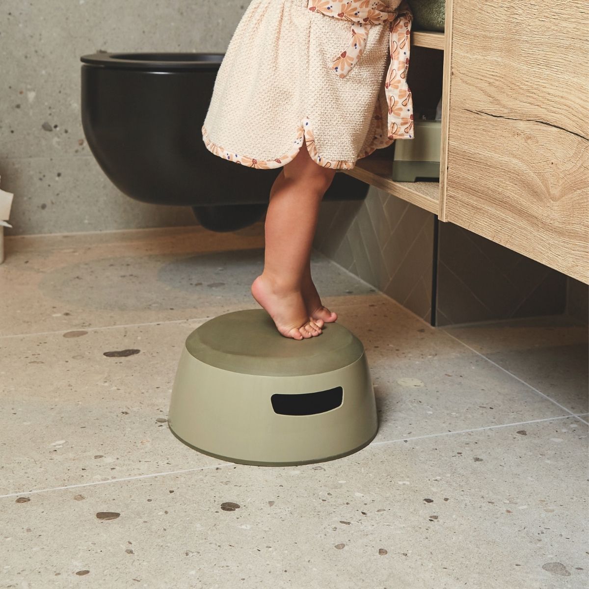 Child's foot on a green step stool in a bathroom setting.