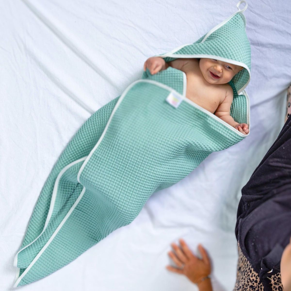Baby wrapped in a green hooded towel on a white bed